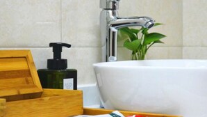 Une salle de bain avec une baignoire blanche, un plateau en bois contenant des articles de toilette et une bouteille verte de savon pour les mains EAAE.