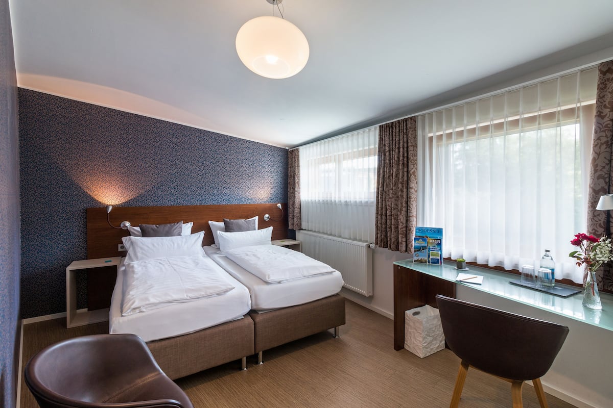 Habitación de hotel con cama doble, escritorio, silla y ventana con cortinas.