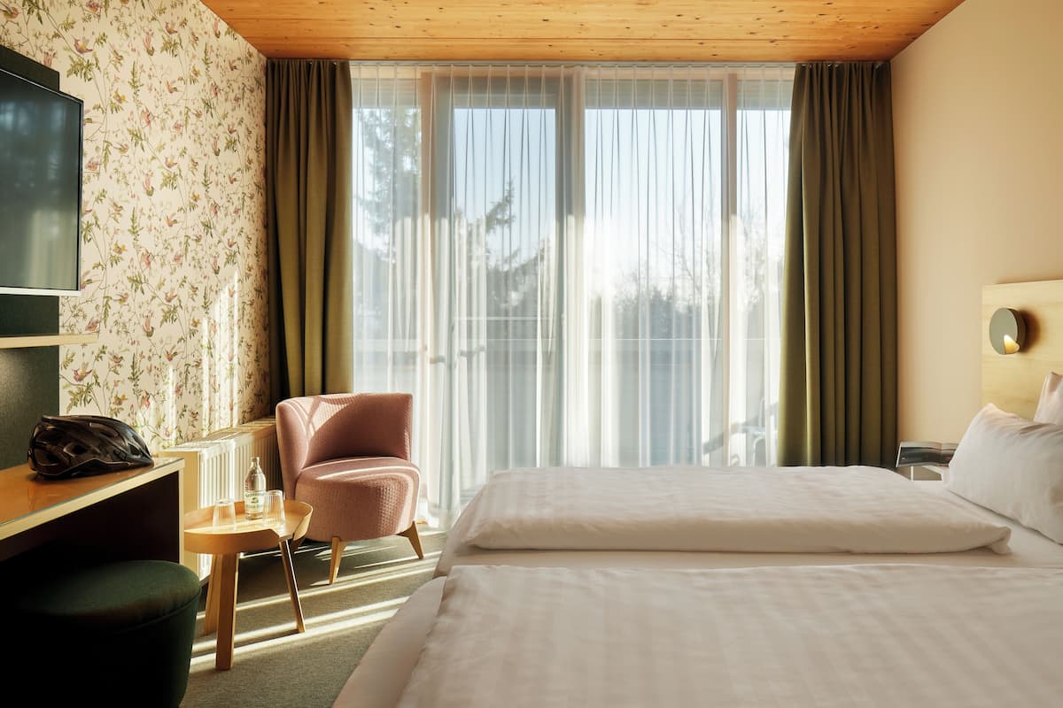 Una habitación de hotel con cama, escritorio, silla, televisor y ventana con cortinas.