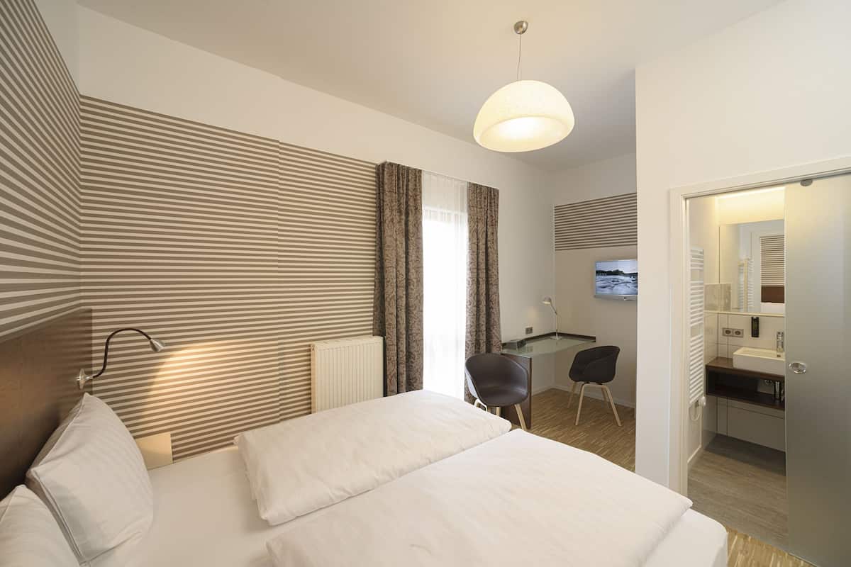 Habitación de hotel con una cama grande, un escritorio, una silla, un televisor y un baño.