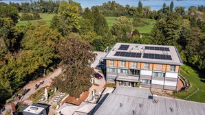 A hotel with a solar panel roof, surrounded by trees and a view of a lake.