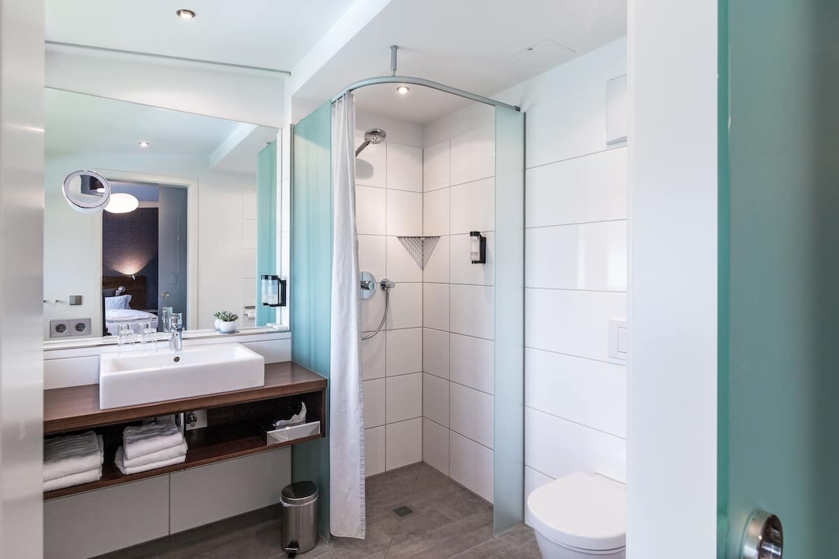 Un baño moderno con lavamanos, espejo y ducha blancos.