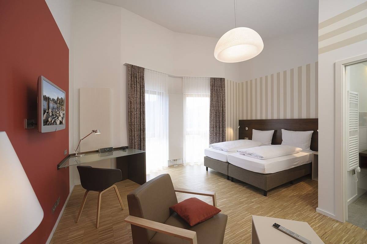 Una habitación de hotel con cama, escritorio, silla y televisor en la pared.