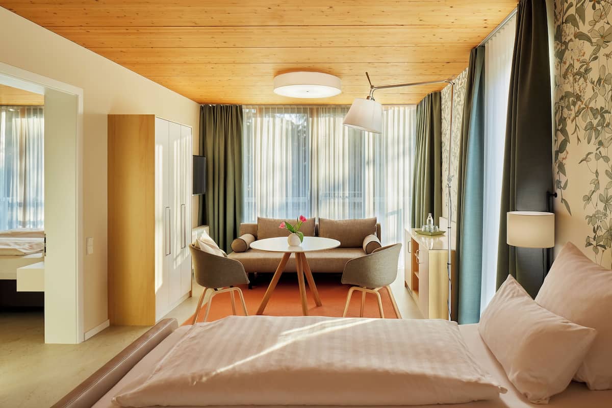 Una habitación de hotel con una cama, una mesa redonda con sillas, un sofá y cortinas.