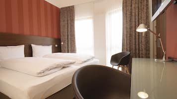 Una habitación de hotel con cama, una silla, un escritorio con lámpara y cortinas.