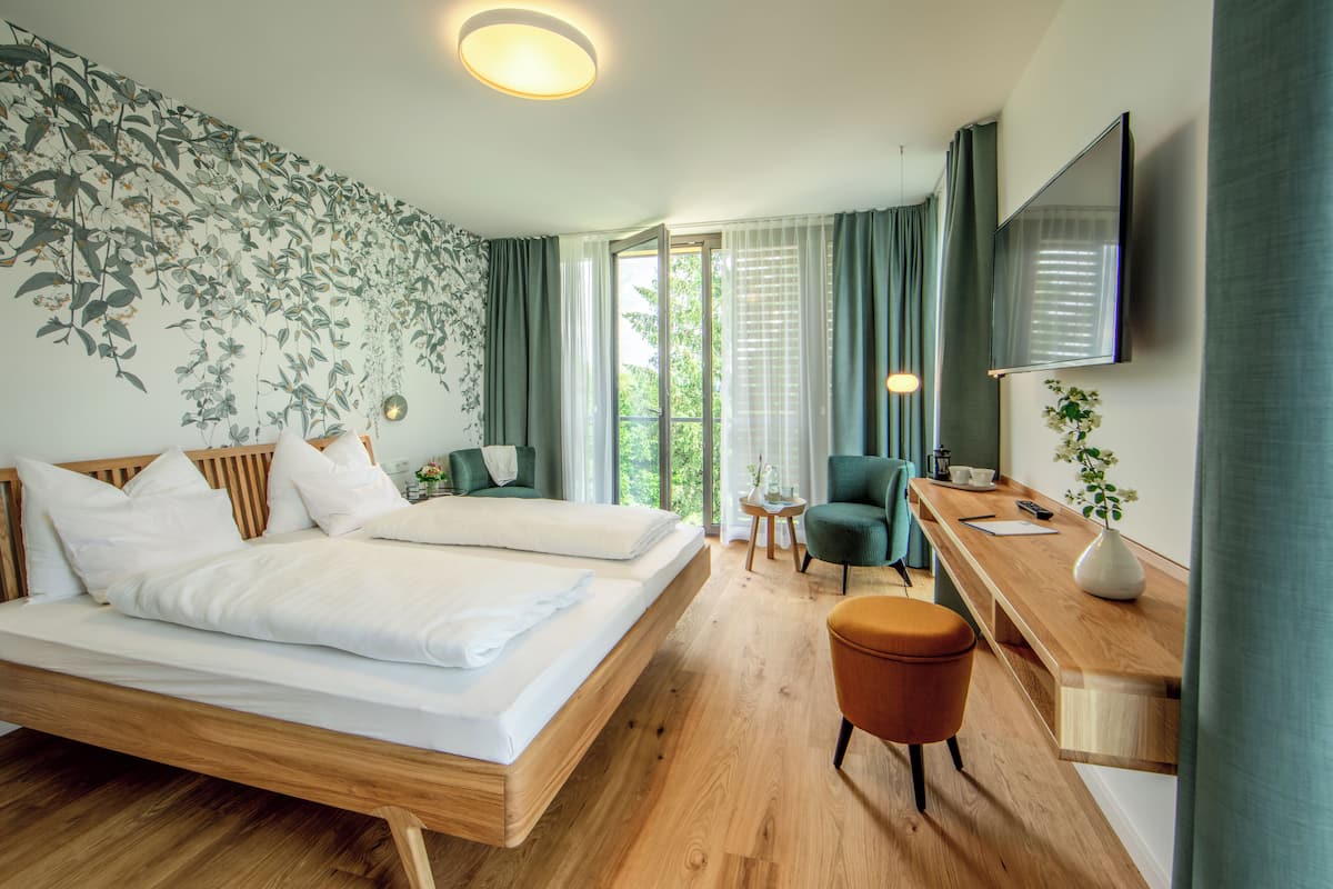 Una habitación de hotel moderna con una cama de madera, un escritorio con silla, un televisor y un ventanal con cortinas.