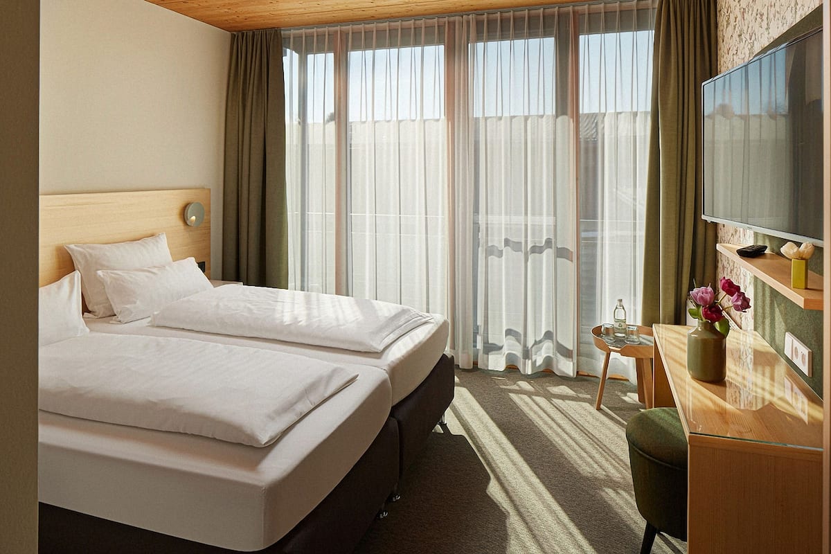 Habitación de hotel con dos camas, un escritorio con televisor y vistas al exterior.