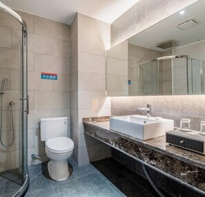 Un baño moderno con ducha de vidrio, inodoro blanco y encimera de mármol con lavamanos y tocador.
