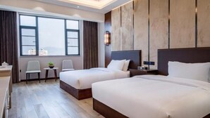 A hotel room with two beds, a desk, a chair, a small table, and a window with a view of buildings. - Vyluk Hotel Jianshui Gucheng (Honghe)