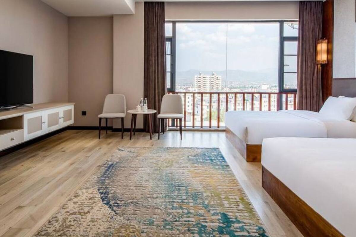 Habitación de hotel con un ventanal grande, televisión, dos camas, un escritorio y una silla.