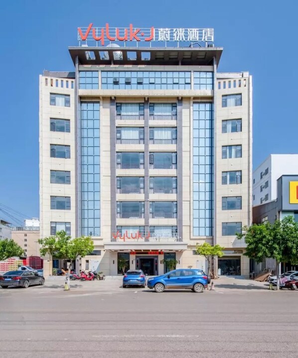 Un moderno edificio de hotel con un letrero claro, varios pisos y un estacionamiento al frente.