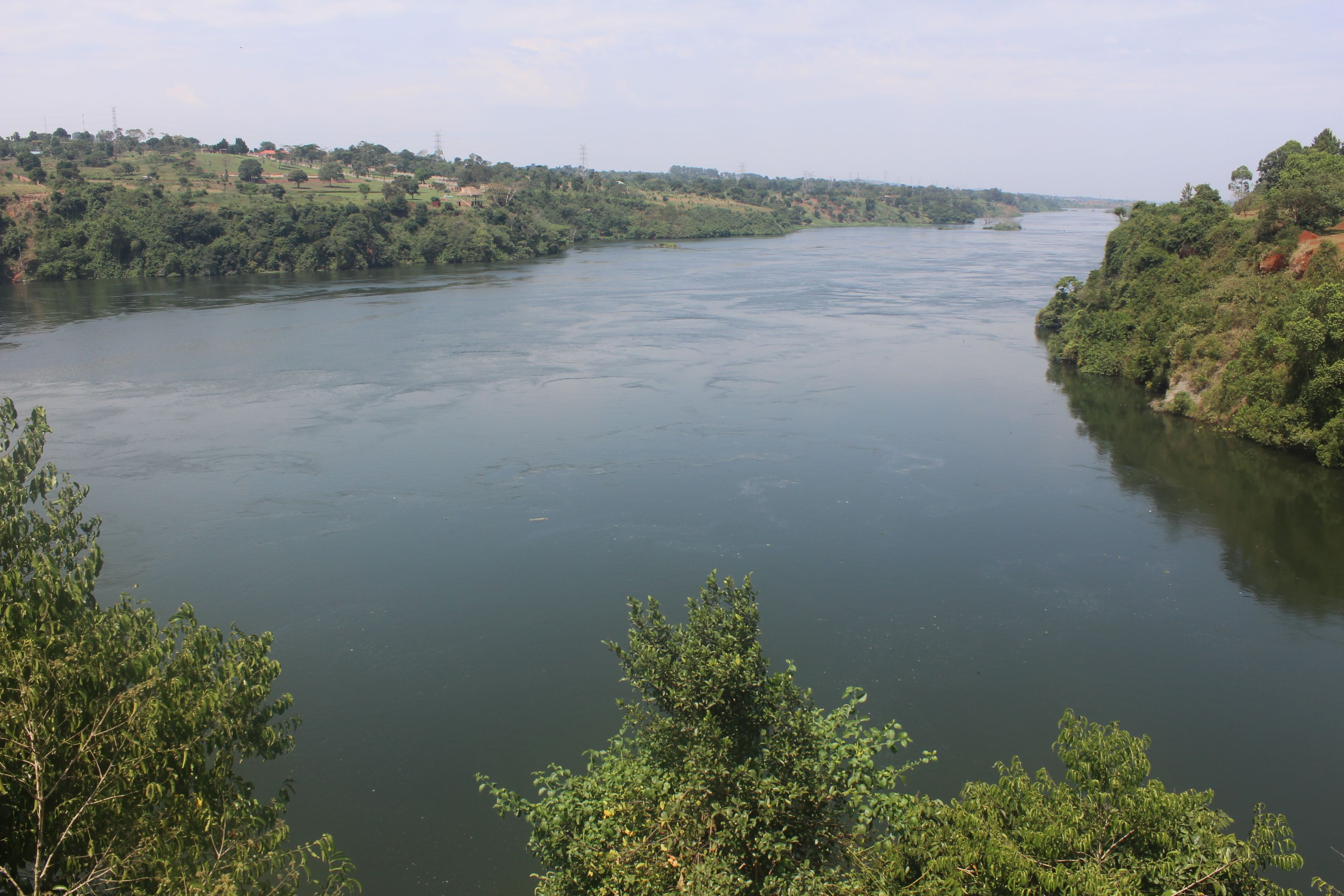 Une rivière bordée de verdure et entourée de collines.