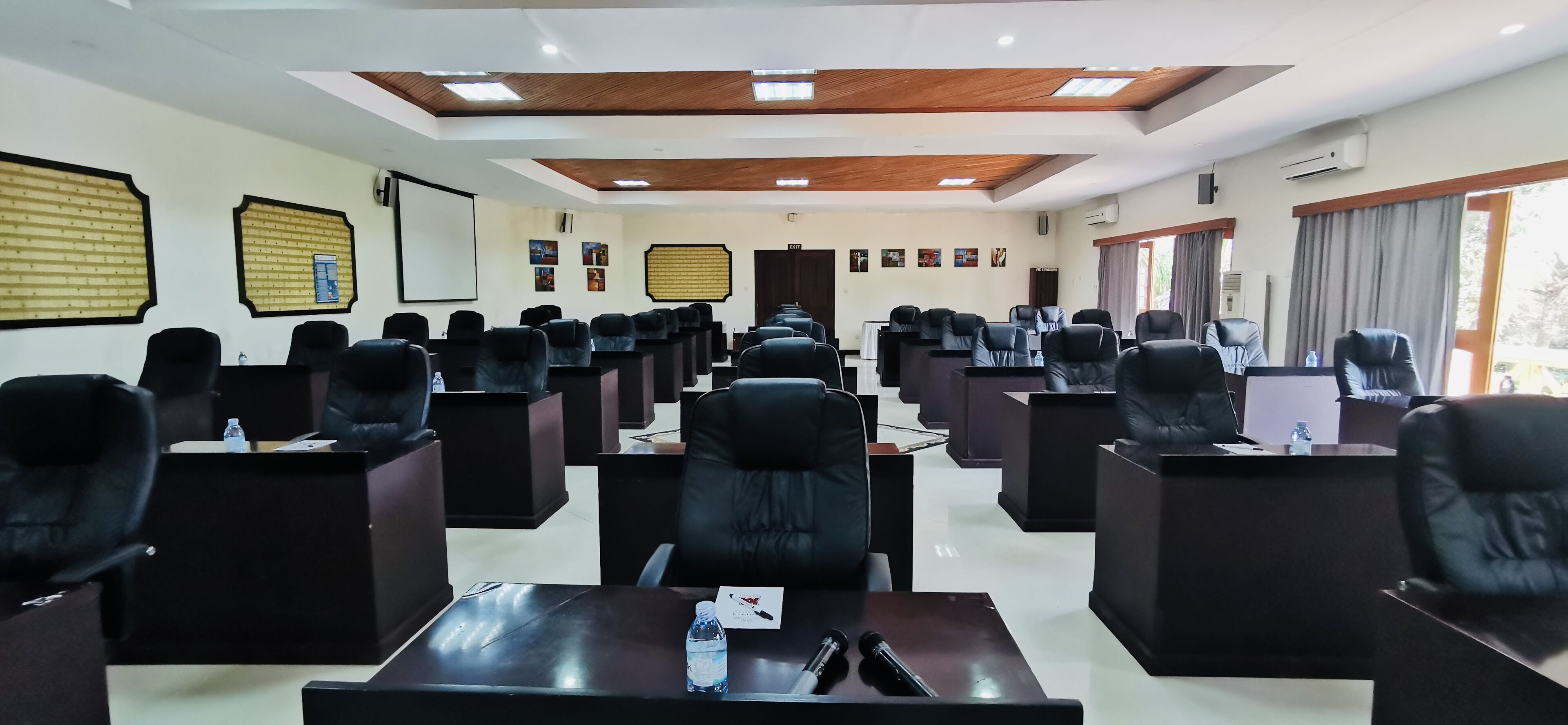 A conference room with multiple black leather chairs arranged in rows, a projector screen, and framed pictures on the walls.