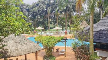 A pool area with lounge chairs and umbrellas, surrounded by lush greenery and palm trees.