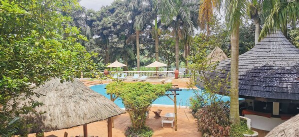 A pool area with lounge chairs and umbrellas, surrounded by lush greenery and palm trees. - Jinja Nile Resort (Jinja)