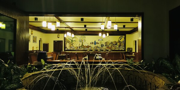 Un restaurante con un mural grande, lámparas colgantes y una fuente de piedra.