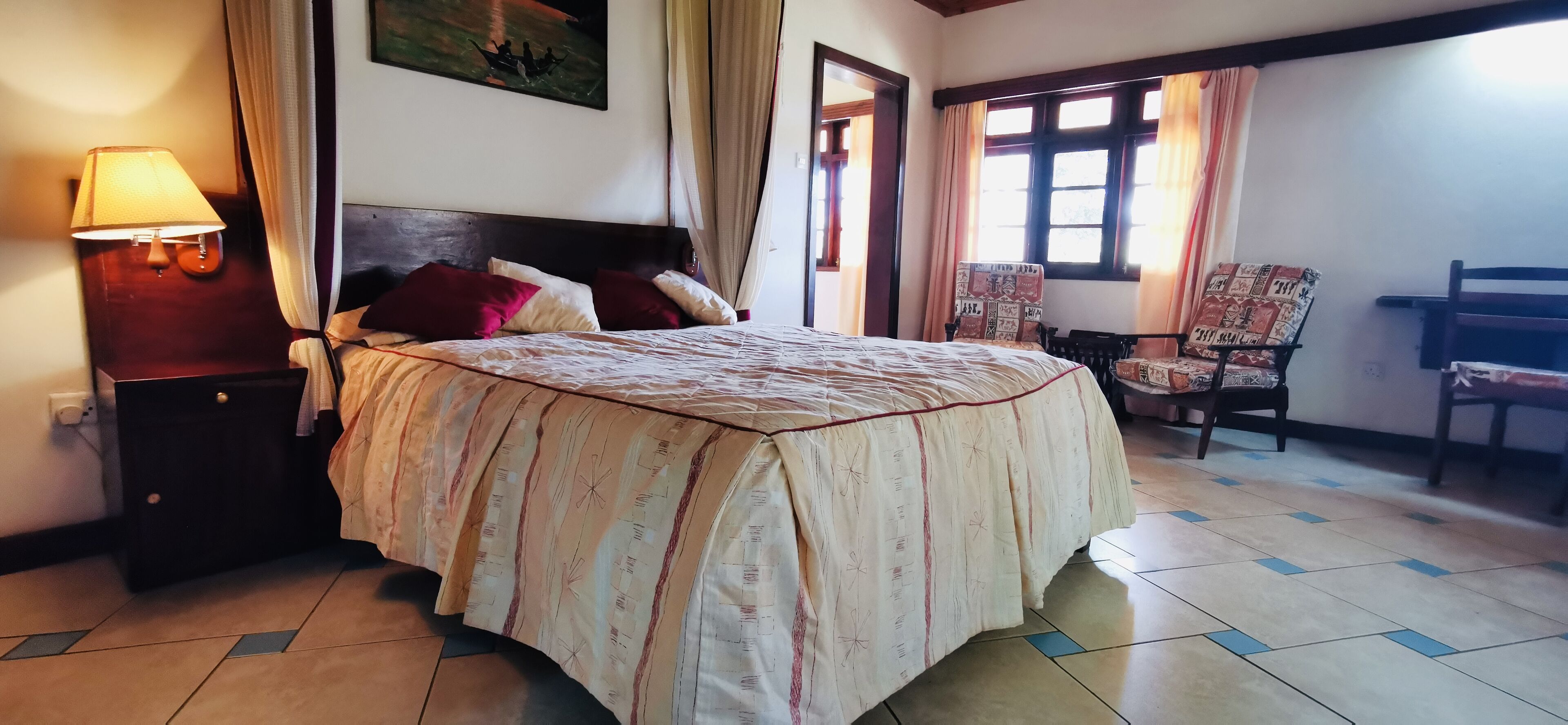Un lit bien fait, avec une couvre-lit à motifs, une lampe de chevet et une chaise agrémentée d’un coussin.