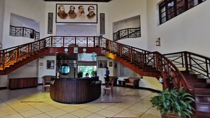 Un vestíbulo con mostrador de recepción central, varias escaleras y un amplio ventanal con vidrieras.