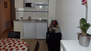 A compact kitchen with a microwave, toaster, and sink. A dining table with a strawberry-patterned tablecloth is visible.
