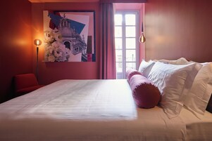 Un dormitorio con una cama grande, una silla roja, una lámpara de pared y una ventana con cortinas.