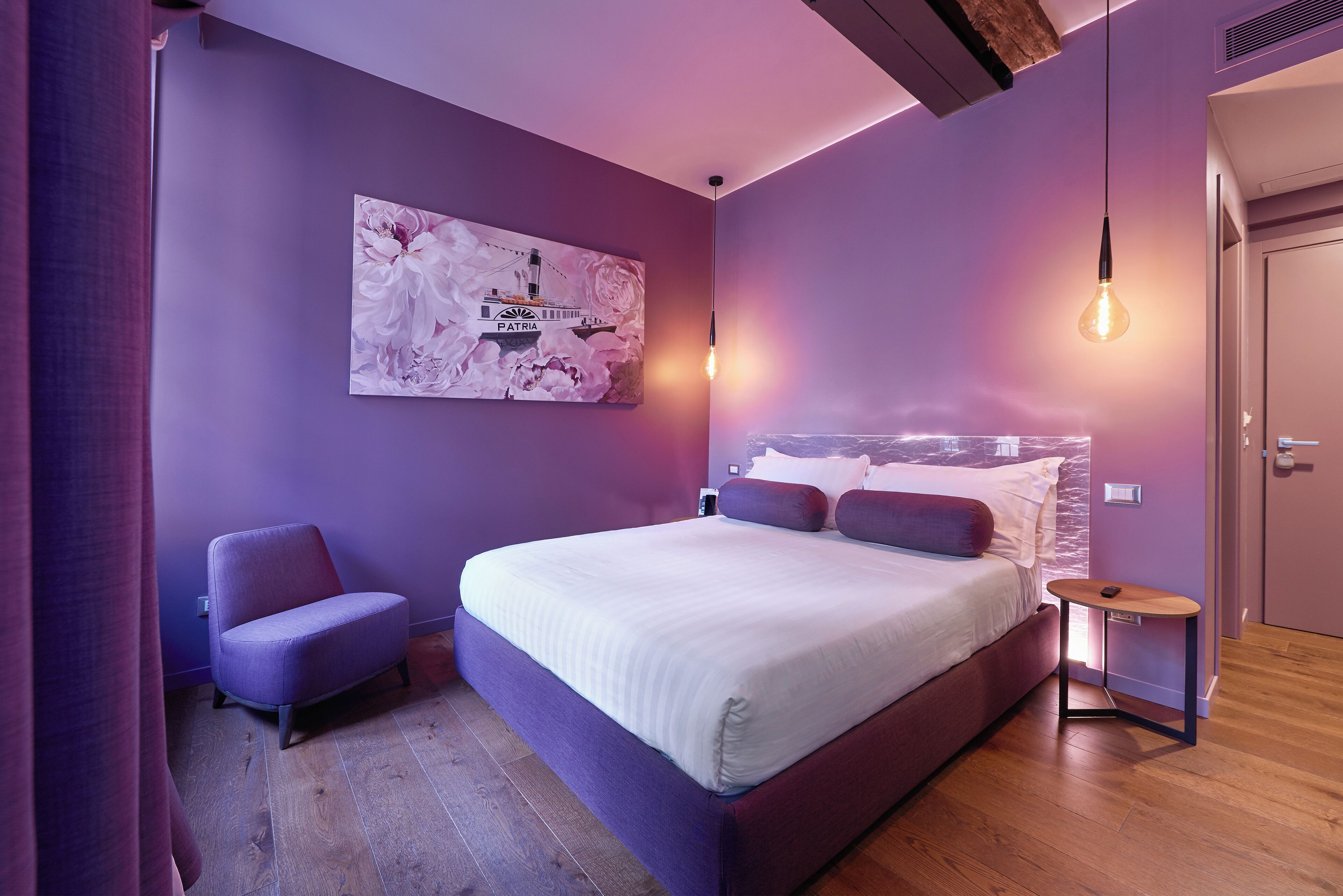 A modern bedroom with a large bed, a small chair, and a nightstand.