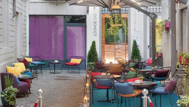 An outdoor seating area with tables and chairs, a red rope barrier, and a sign for "SETTANTARE BOUTIQUE HOTEL". - 73 Boutique Hotel   (Como)