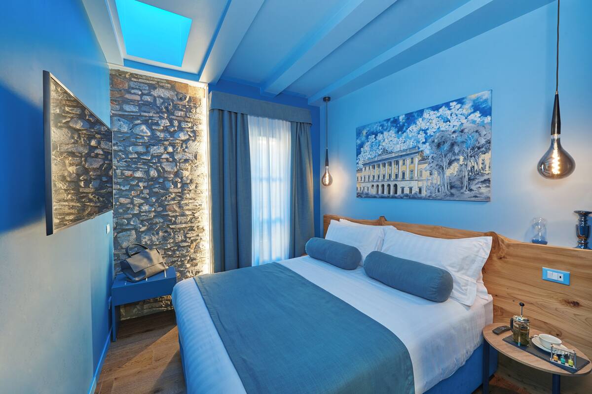 A modern hotel room with a large bed, a stone accent wall, a painting, and a skylight.