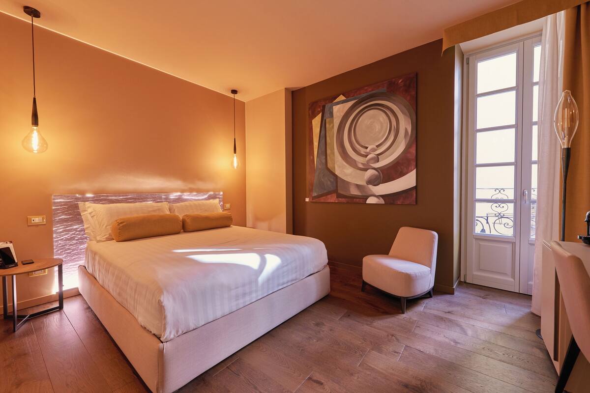 A bedroom with a large bed, a bedside table, a chair, and a painting on the wall.