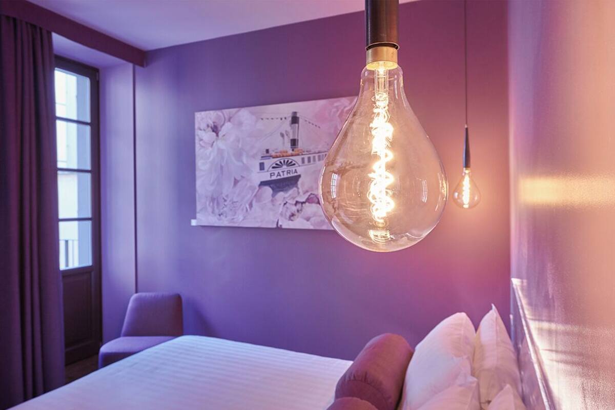 A hotel room with a bed, a hanging light fixture, and a wall-mounted artwork.