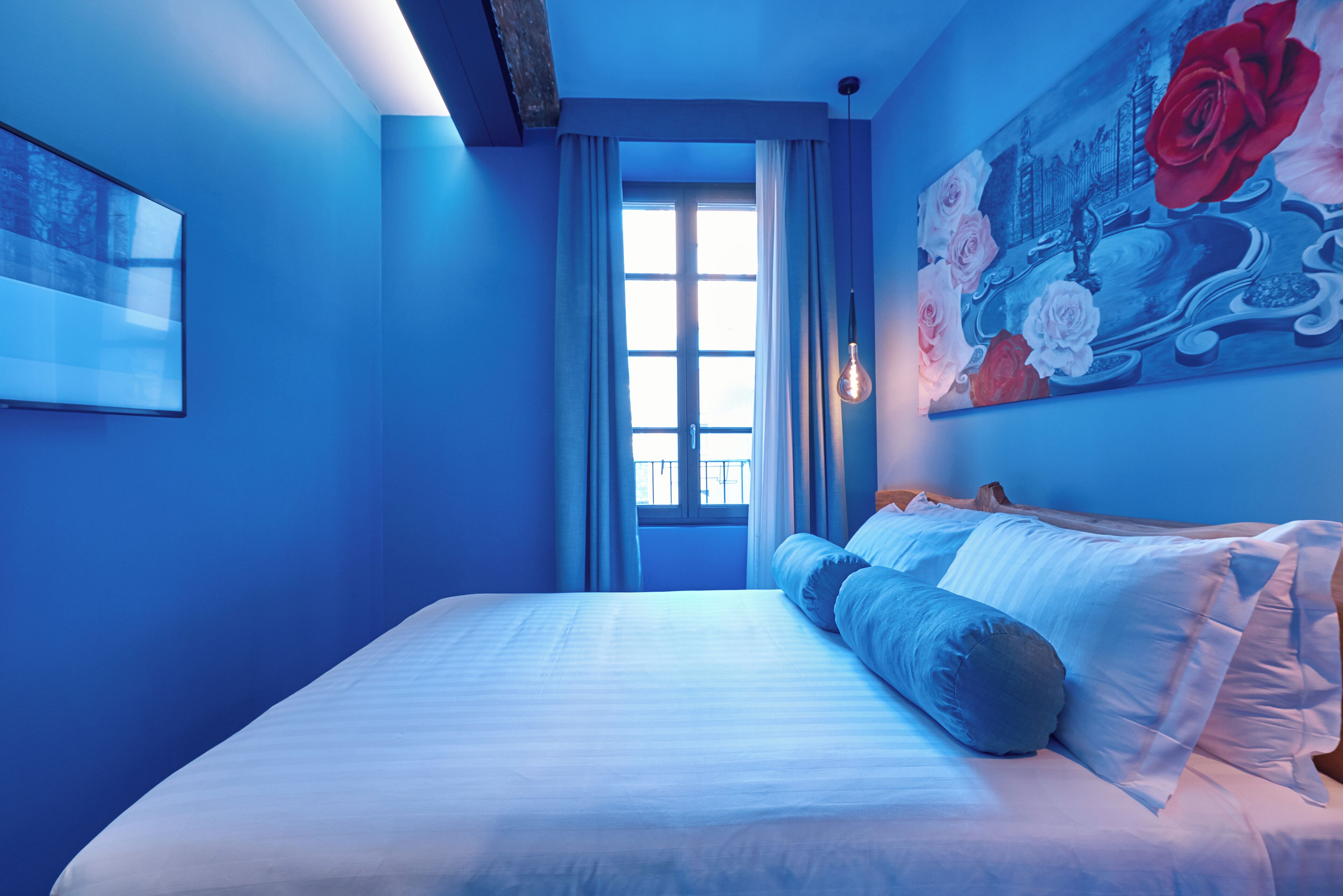 Een slaapkamer met een groot bed, een raam met gordijnen, een rozenprint en een lamp.