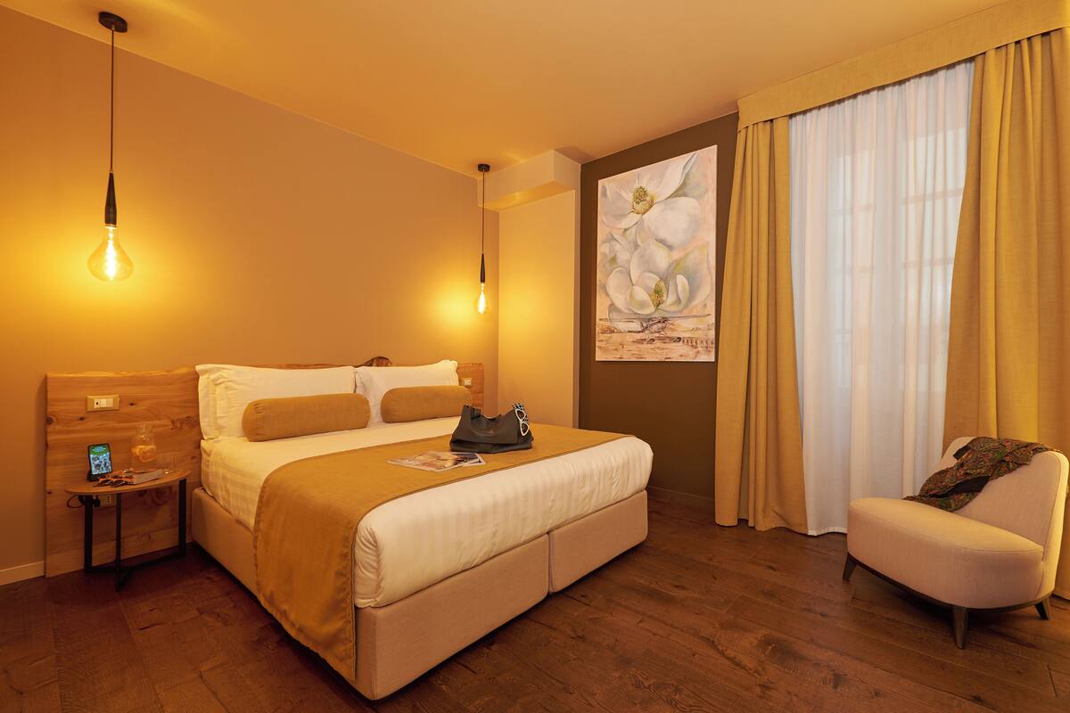 A hotel room with a large bed, a nightstand, a chair, and a painting on the wall.