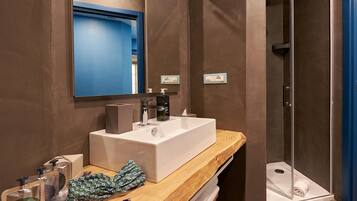 A bathroom with a large white sink, a mirror, a shower, and a wooden vanity.