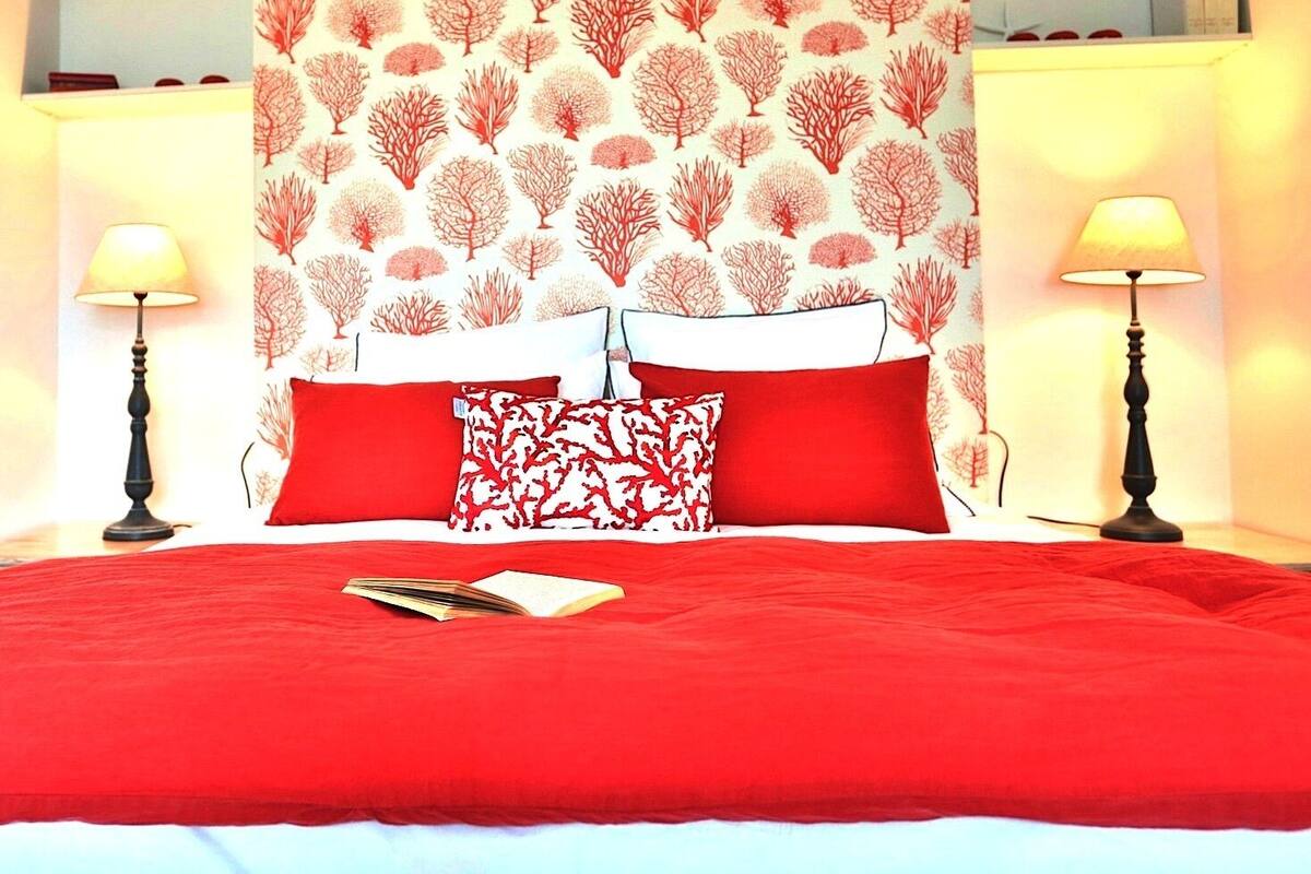 Ein Bett mit roter Bettwäsche, zwei Kissen, ein Buch und eine Wand mit einem Baummuster.
