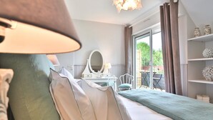 A hotel room with a bed, a bedside table with a lamp, a mirror, and a view of the outdoors through a large window. - Rêves de Bord de Mer (Locmariaquer)