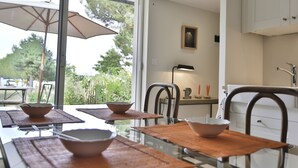 A modern dining area with a glass table, brown placemats, and a white umbrella. - Rêves de Bord de Mer (Locmariaquer)
