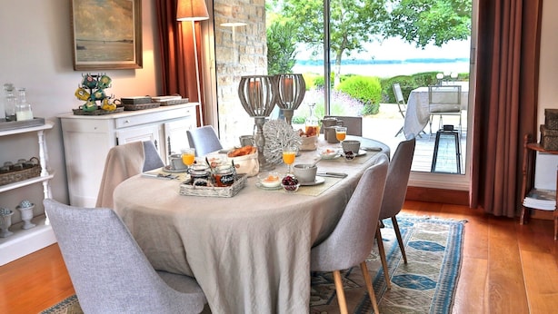 A dining area with a table set for breakfast, a view of the outdoors, and a stone wall. - Rêves de Bord de Mer (Locmariaquer)