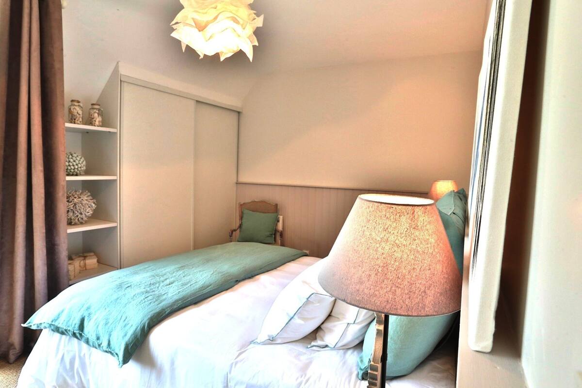 Ein Schlafzimmer mit einem Bett, einem Nachttisch, einer Lampe, einem Regal mit Dekoration und einem Kleiderschrank.