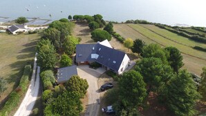 An aerial view of a house with a large lawn, a driveway, and a body of water in the background. - Rêves de Bord de Mer (Locmariaquer)
