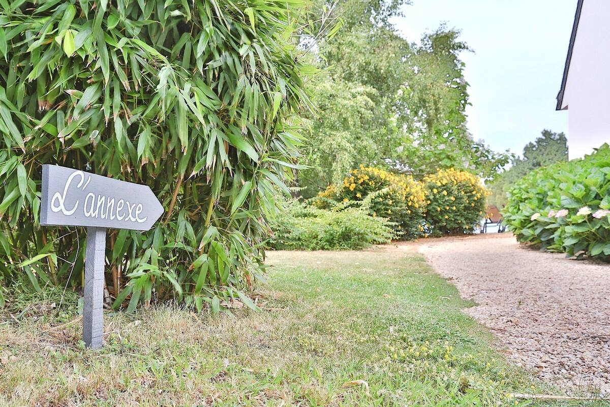Ein Schild mit der Aufschrift 'L'annexe' in einem Garten mit üppiger Bepflanzung und einem Kiesweg.