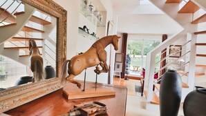 A spacious room with a wooden horse sculpture, a large ornate mirror, and a staircase with a modern design. - Rêves de Bord de Mer (Locmariaquer)