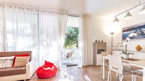 Ein modernes Wohnzimmer mit einer Couch, einem Esstisch mit Stühlen, einem roten Sitzsack und Blick durch ein großes Fenster.