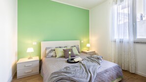 Ein ordentlich bezogenes Bett mit einer grauen Decke, zwei Nachttischlampen und einem Nachttisch mit Lampe.