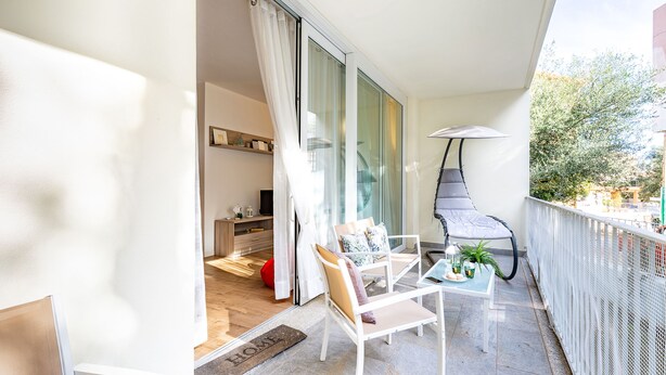 Ein Balkon mit einem weißen Stuhl, einem kleinen Tisch mit einer Pflanze und einem roten Sitzsack.