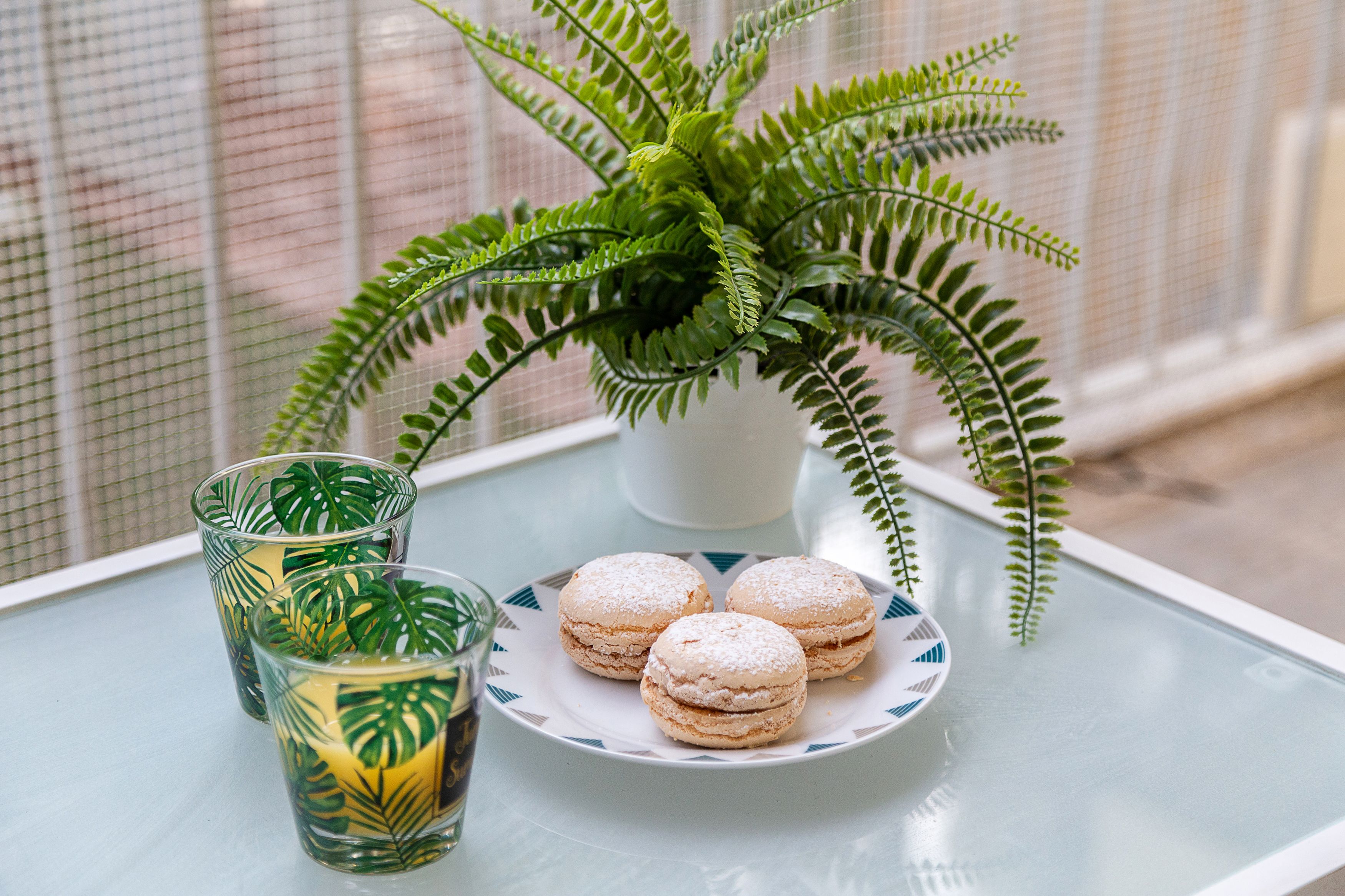 A table with a glass of iced tea, a plate of macarons, and a potted fern.