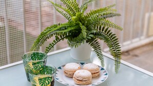 Ein Tisch mit einem Glas Eistee, einer Platte Macarons und einem Blumentopf mit einem Farn.