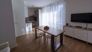 A modern kitchen with a wooden table, two stools, a TV, and a large window with curtains. - Casa Selvaggio Blu (Baunei)
