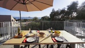 A dining table set outdoors with a view of the sea, surrounded by a white metal fence. - Casa Selvaggio Blu (Baunei)