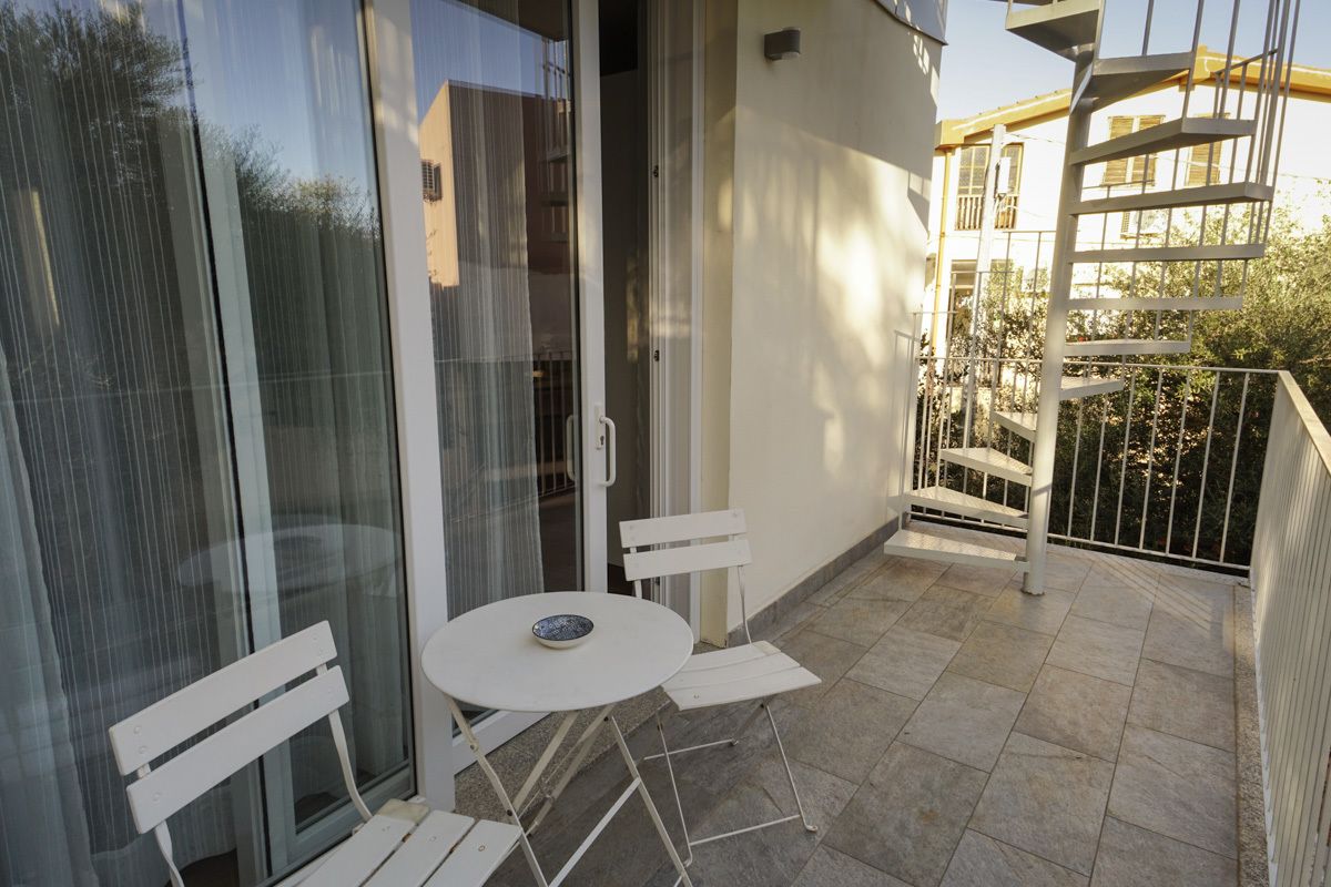 Een balkon met een witte tafel en stoelen, een glazen deur en een metalen spiltrap.