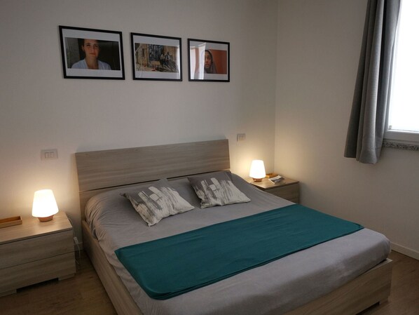 Una cama bien hecha con un edredón azul aguamarina, dos lámparas de noche y tres cuadros en la pared.