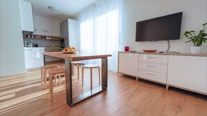 A modern kitchen with a wooden table, two stools, a TV, and a potted plant. - Casa Selvaggio Blu (Baunei)